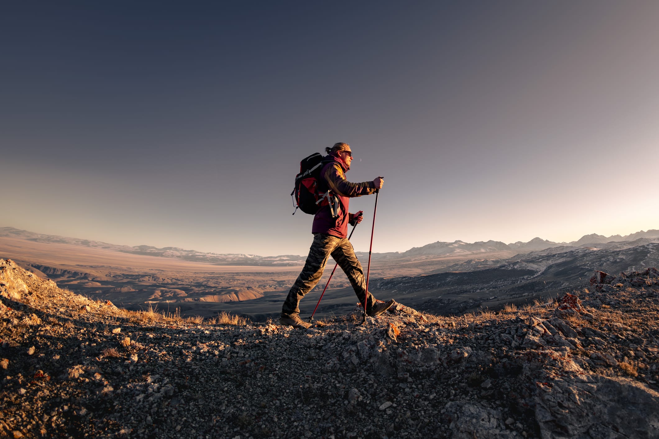 Hiker man with backpack walks high in mountains at sunset