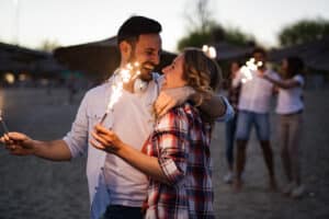 Happy group of friends lighting sparklers and enjoying freedom at beach during sunset