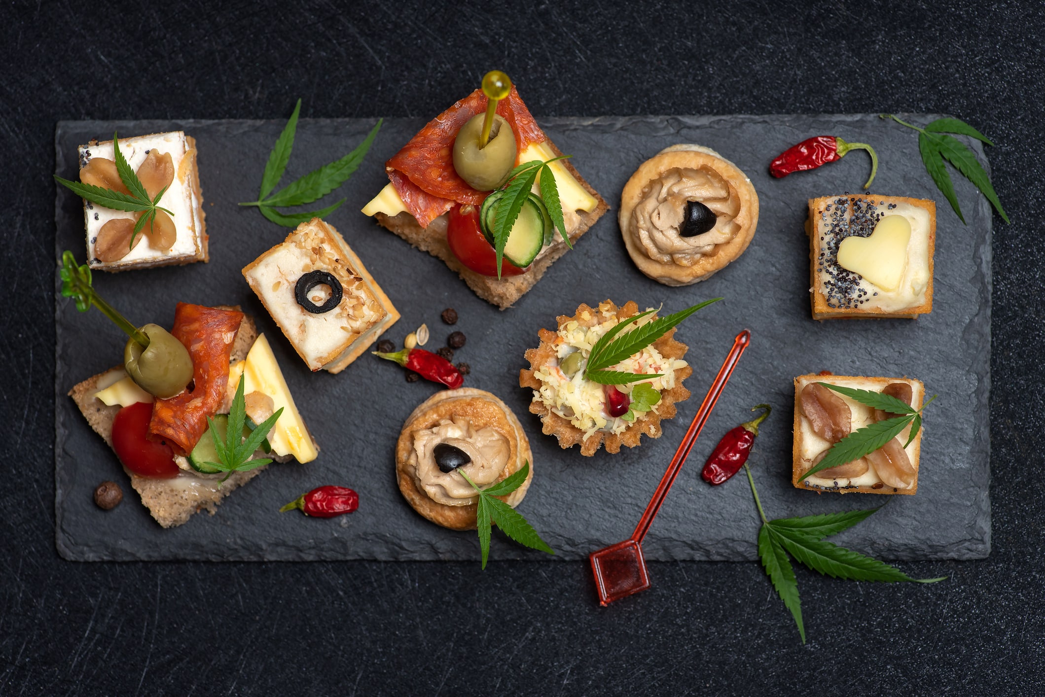 Canapés with different toppings on a black serving board on a black background.