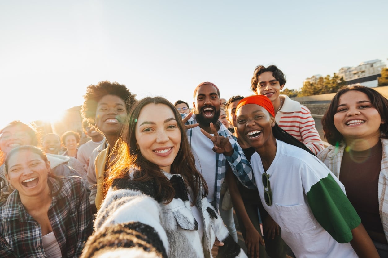 A group of happy and diverse young adults smiling together outdoors in the sunlight, capturing a moment of connection and friendships. The atmosphere radiates joy, excitement, and unity.