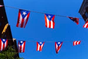 Puerto Rican flags waving in the wind against a clear blue sky with sunlight shining through.