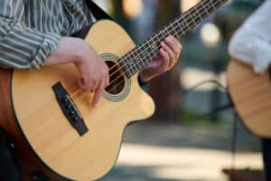 Man playing acoustic bass guitar at outdoor event, close up view to wooden guitar neck. Right handed bass player man playing four strings bass guitar, very nimble fingers of street music artist
