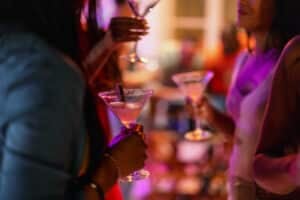 Close-up of a martini glass held by a female at a bar with purple lighting. Delicious summer cocktail.